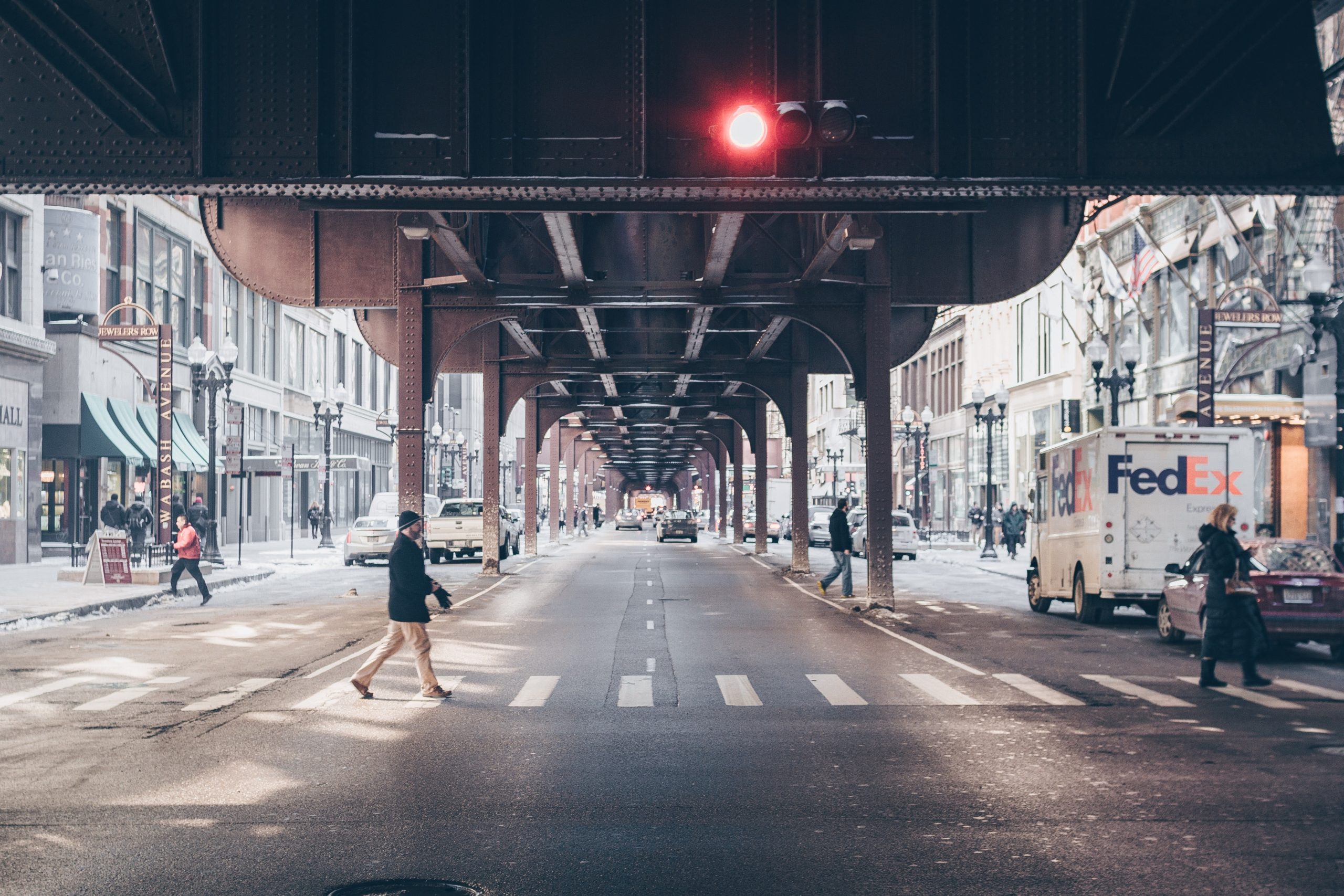 Pedestrian crossing a city street beneath an elevated railway in Chicago